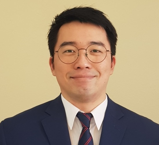Male looks at camera, closed mouth smile. Short black hair, glasses, and suit and tie.