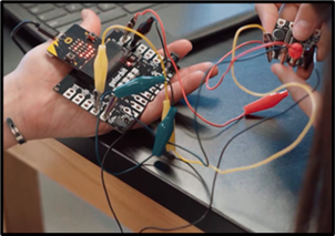 Image shows a hand holding the micro:bit inserted into the Gator:bit with alligator-clip wires connecting the gator:bit to the microphone sensor.