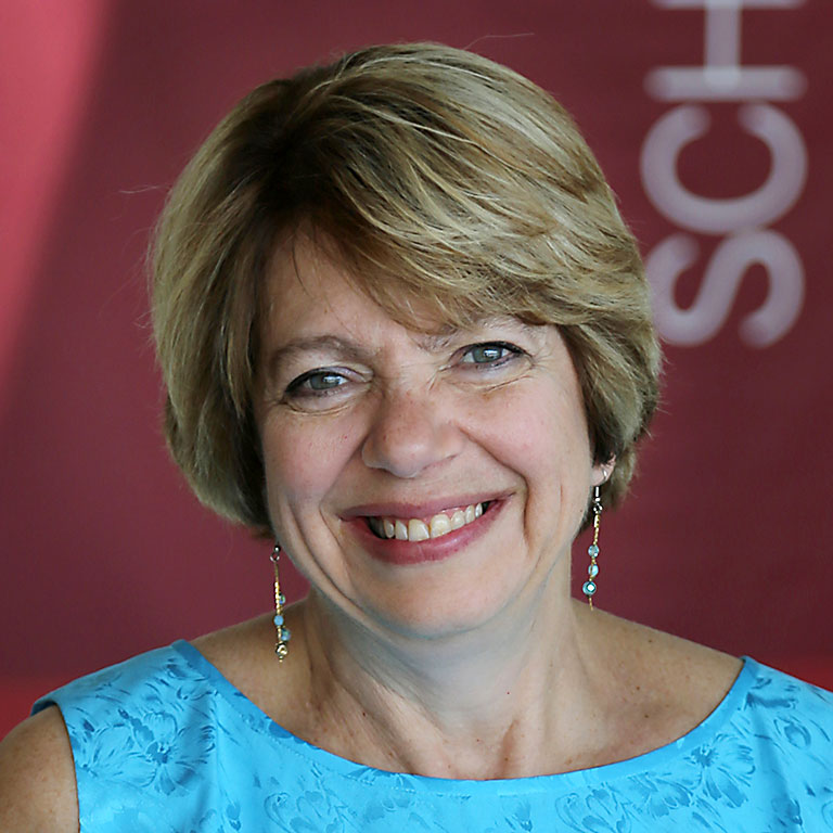 woman with short blonde hair looks at camera. Wears light blue top and long earrings.