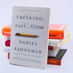 Stack of books with "Thinking fast and slow" book by Daniel Kahneman in front