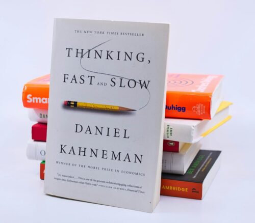 Stack of books with "Thinking fast and slow" book by Daniel Kahneman in front